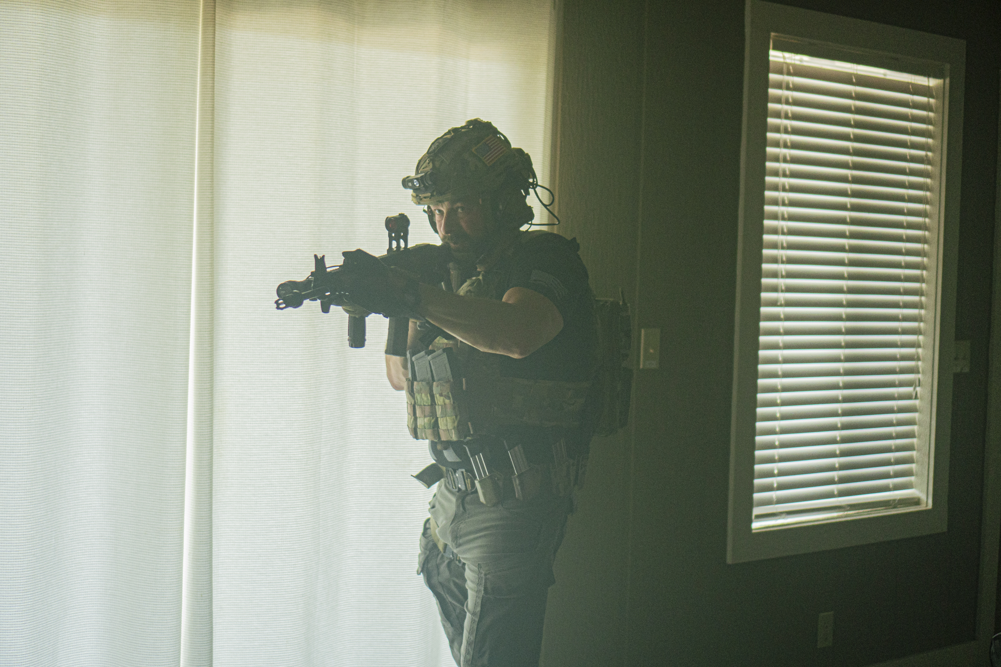 Man in full tactical gear holding an AR15 inside a house